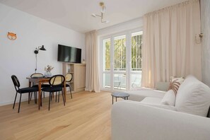Una sala de estar moderna con sofá, mesa de comedor, sillas, televisor y ventanas grandes con cortinas.