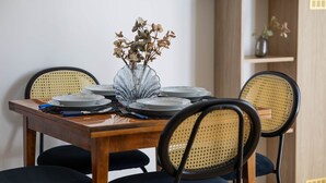 Une table à manger dressée avec des assiettes, un vase contenant des fleurs séchées et des chaises noires au dossier tressé.