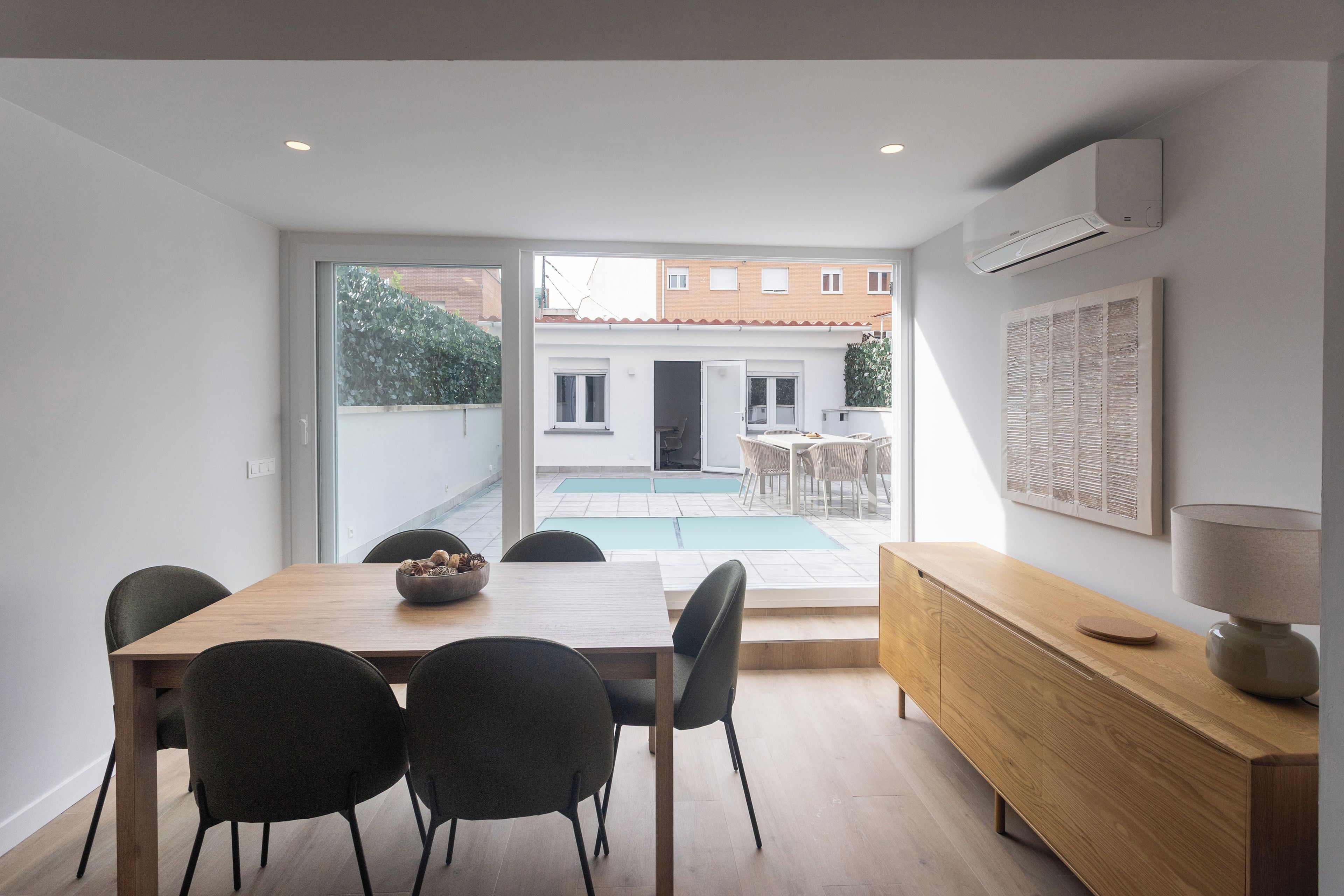 A modern dining area with a wooden table and chairs, a view of a swimming pool, and a large window.