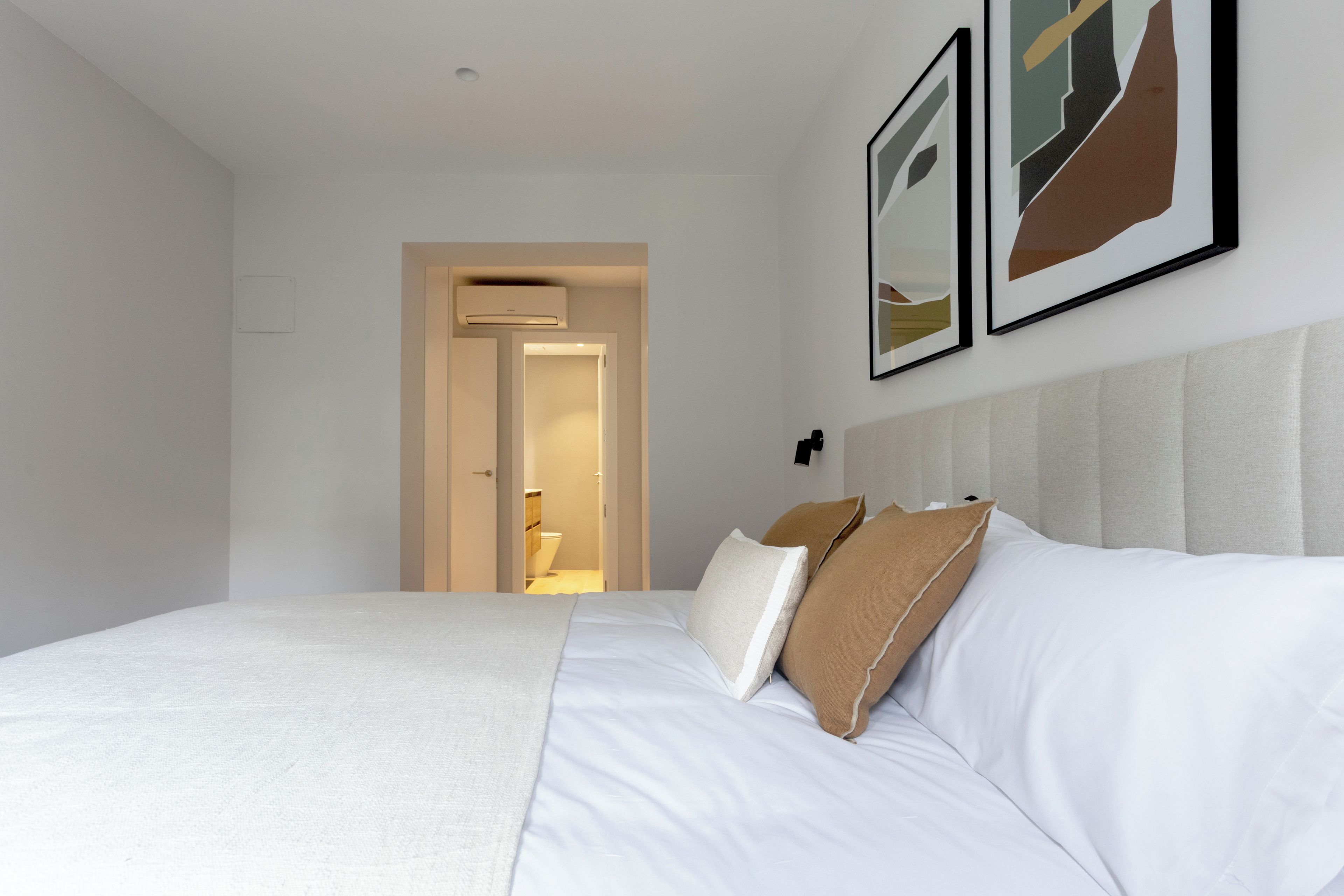 Una camera d'hotel con un letto grande, una testiera, una porta che conduce al bagno e due quadri appesi al muro.