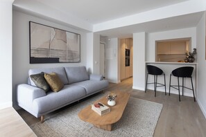 A modern living room with a grey sofa, a coffee table, and a kitchen area with two black bar stools. - A three-bedroom in Tetuán with its own outdoor space and a separate guest house with a workspace, near La Ventilla park and the Castellana. (MADRID)
