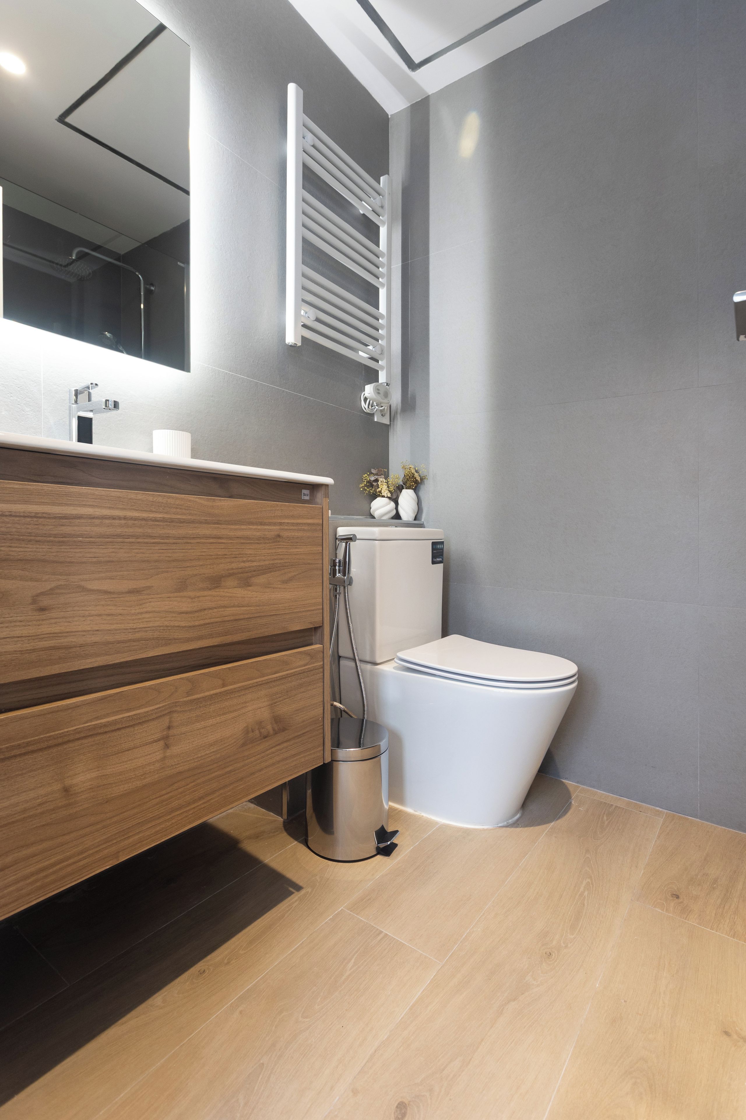 Een moderne badkamer met een houten wastafelmeubel, een wit toilet en een spiegel boven de wastafel.