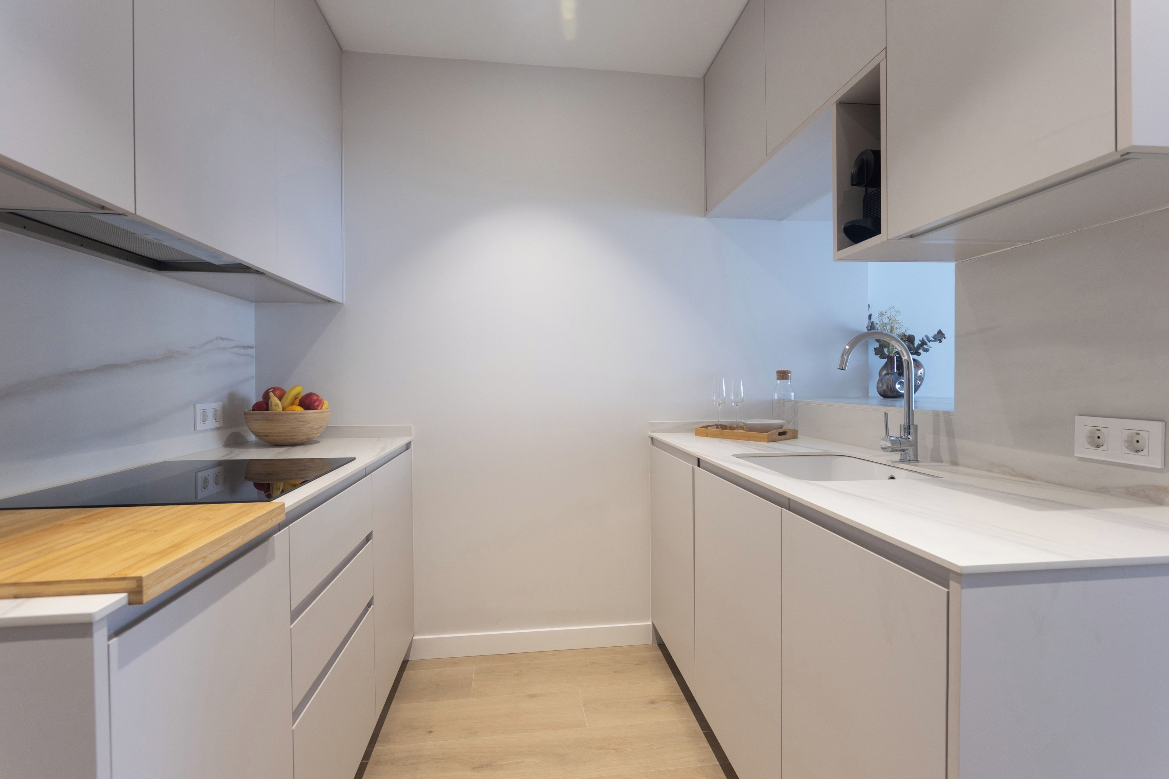 A modern kitchen with white cabinetry, a wooden countertop, a stainless steel sink, and a fruit bowl.
