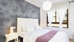 Una camera da letto moderna con un letto grande, un comodino con una lampada e vista all'esterno attraverso tende leggere.