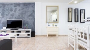 Un soggiorno moderno con televisore piatto, arredi bianchi, un grande specchio e quadri appesi alle pareti.