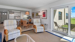 A modern living room with striped armchairs, a dining area, and a kitchen. - Seaward B101 (New Smyrna Beach)