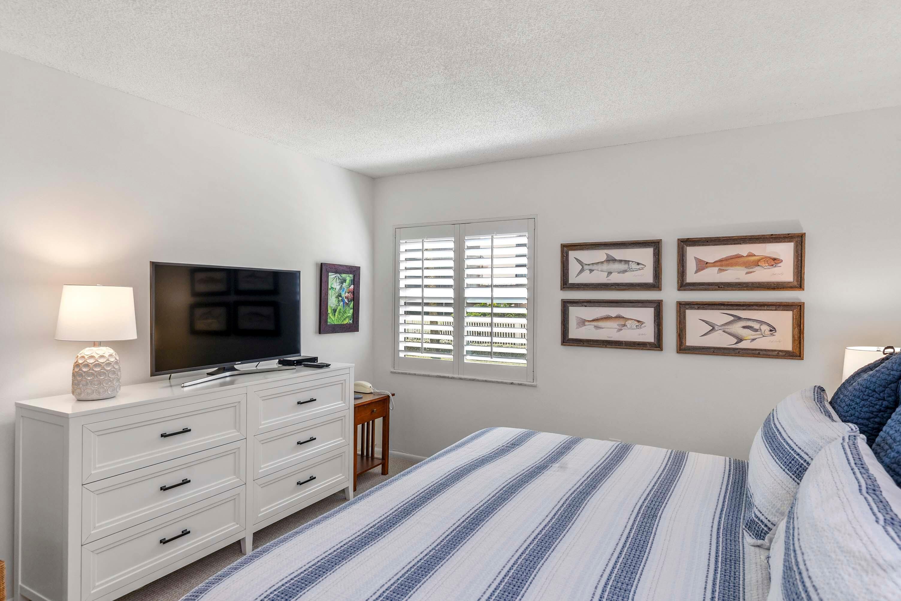 Un dormitorio con cama, televisor en una cómoda, lámpara y cuadros de peces en la pared.