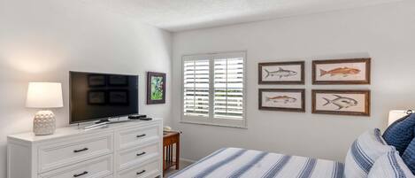 Un dormitorio con cama, televisor en una cómoda, lámpara y cuadros de peces en la pared.