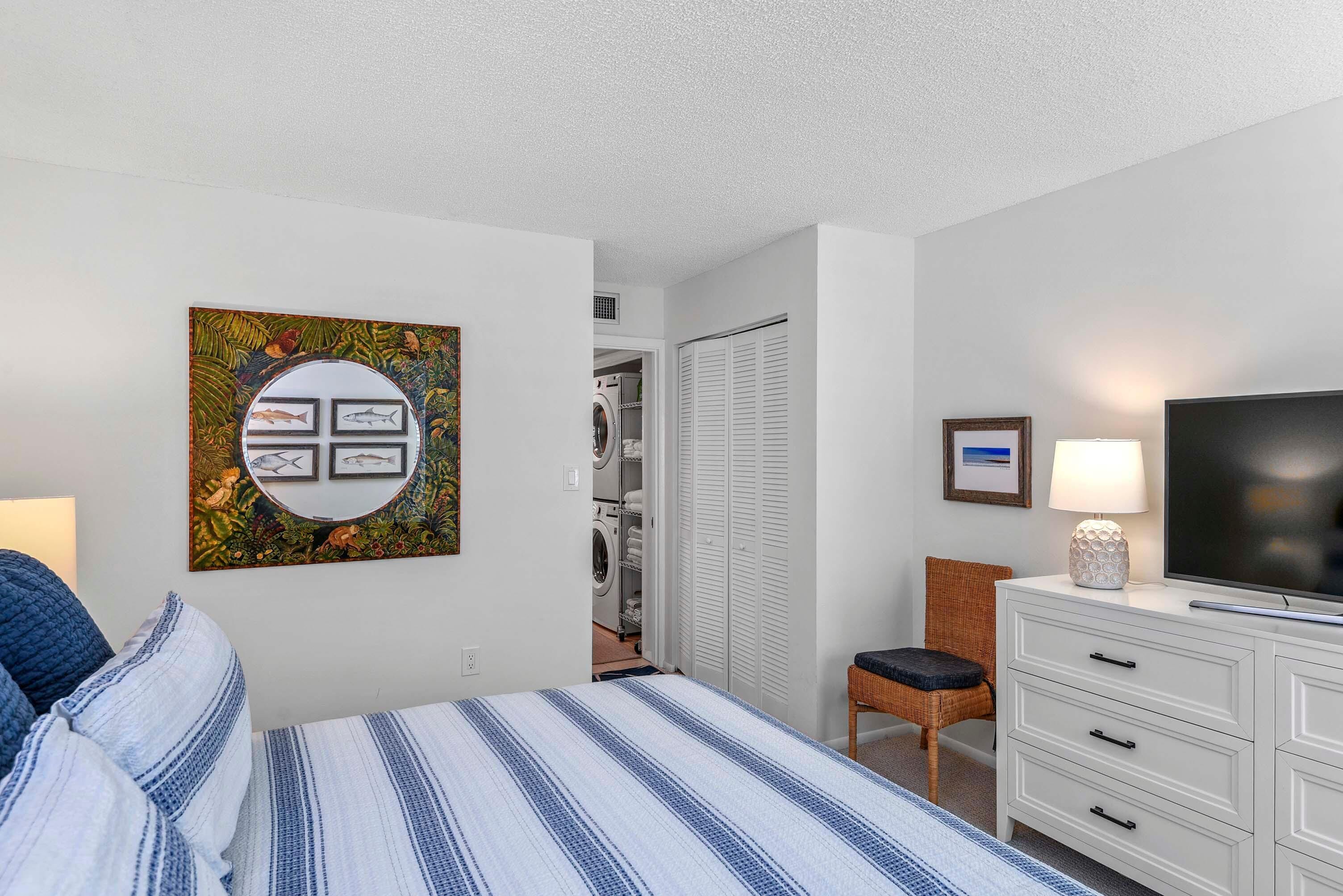 A bedroom with a bed, a TV, a dresser, a chair, and a wall art piece.