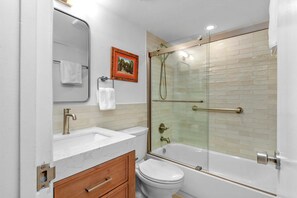 A bathroom with a white sink, a toilet, a bathtub, and a glass-enclosed shower. - Seaward B101 (New Smyrna Beach)