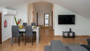 A modern living room with a dining area, a flat-screen TV mounted on the wall, and a fire extinguisher on the wall. - 2-bed apt with sea view |Ponta do Sol SeaView (Socorro)
