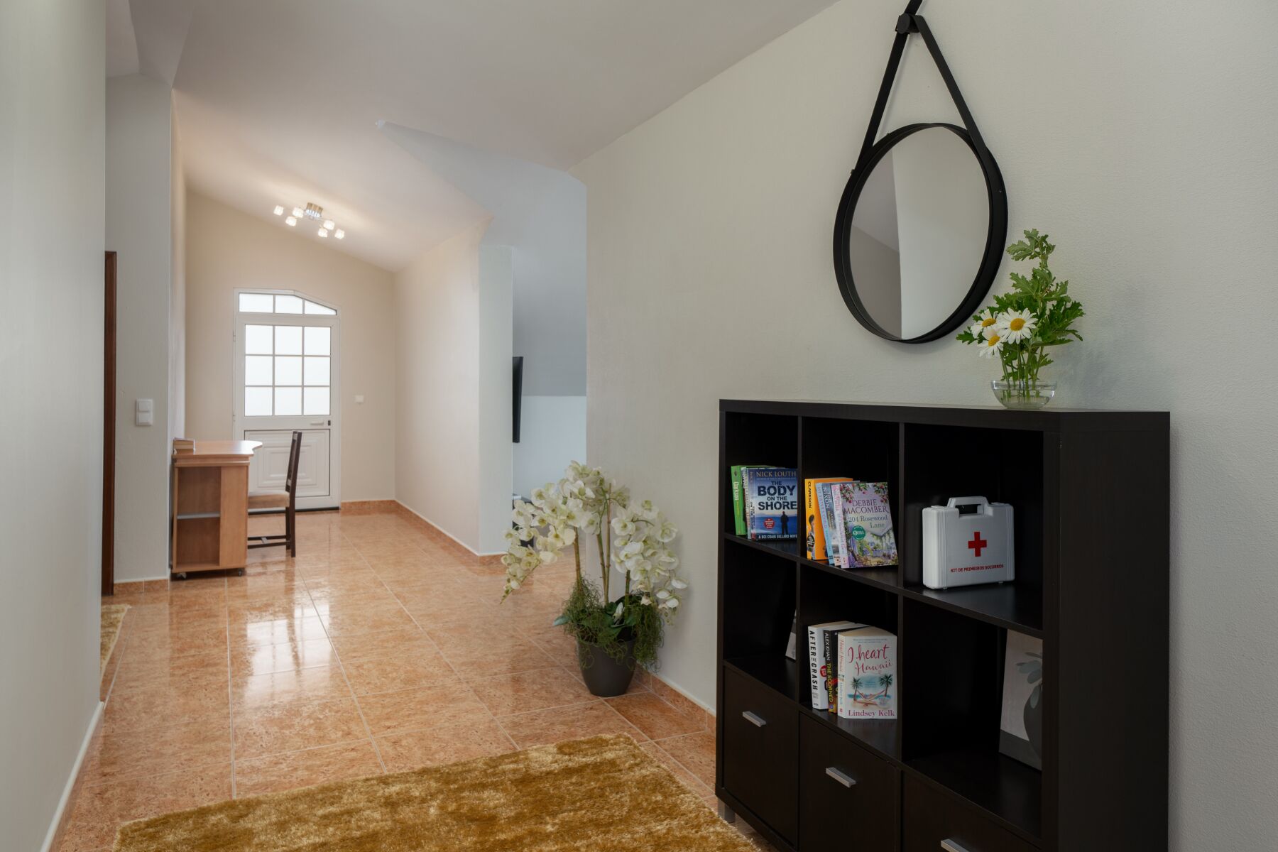 A hallway with a dark wooden cabinet, a potted plant, and a hanging ring light.