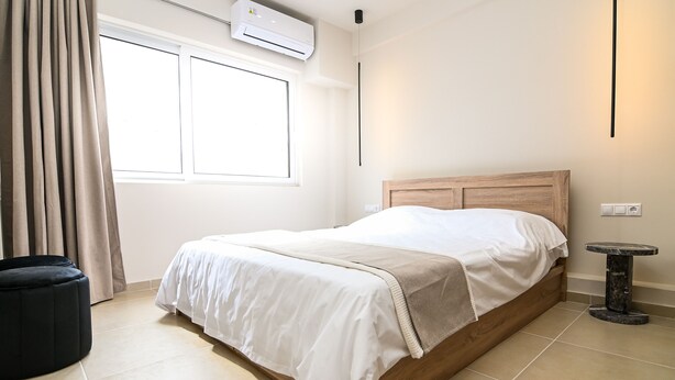 Un dormitorio ordenado con una cama, una mesita redonda y un otoman negro.
