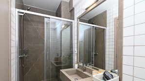 Un baño moderno con ducha envuelta en vidrio, un espejo grande y un tocador con lavabo y espacio de almacenamiento.