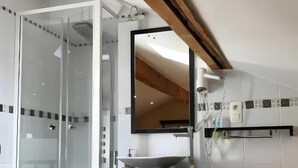 Een moderne badkamer met een douchecabine van glas, een witte wastafel met een wastafel en een spiegel erboven.