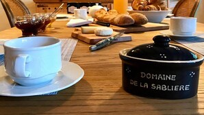 Une table de petit-déjeuner avec des croissants, une bouteille de jus d’orange, une tasse de café et un pot en céramique portant l’inscription « Domaine de la Sablière ».