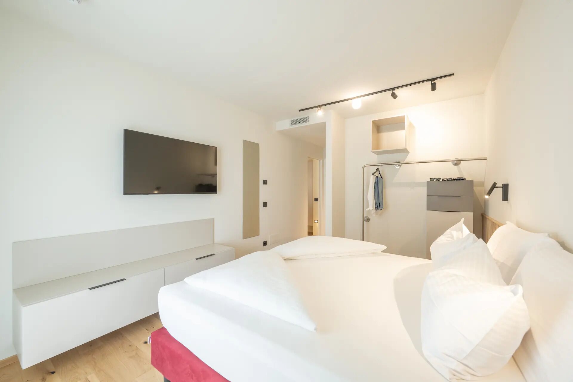 Une chambre à coucher avec un lit, un téléviseur fixé au mur, une armoire et un miroir.