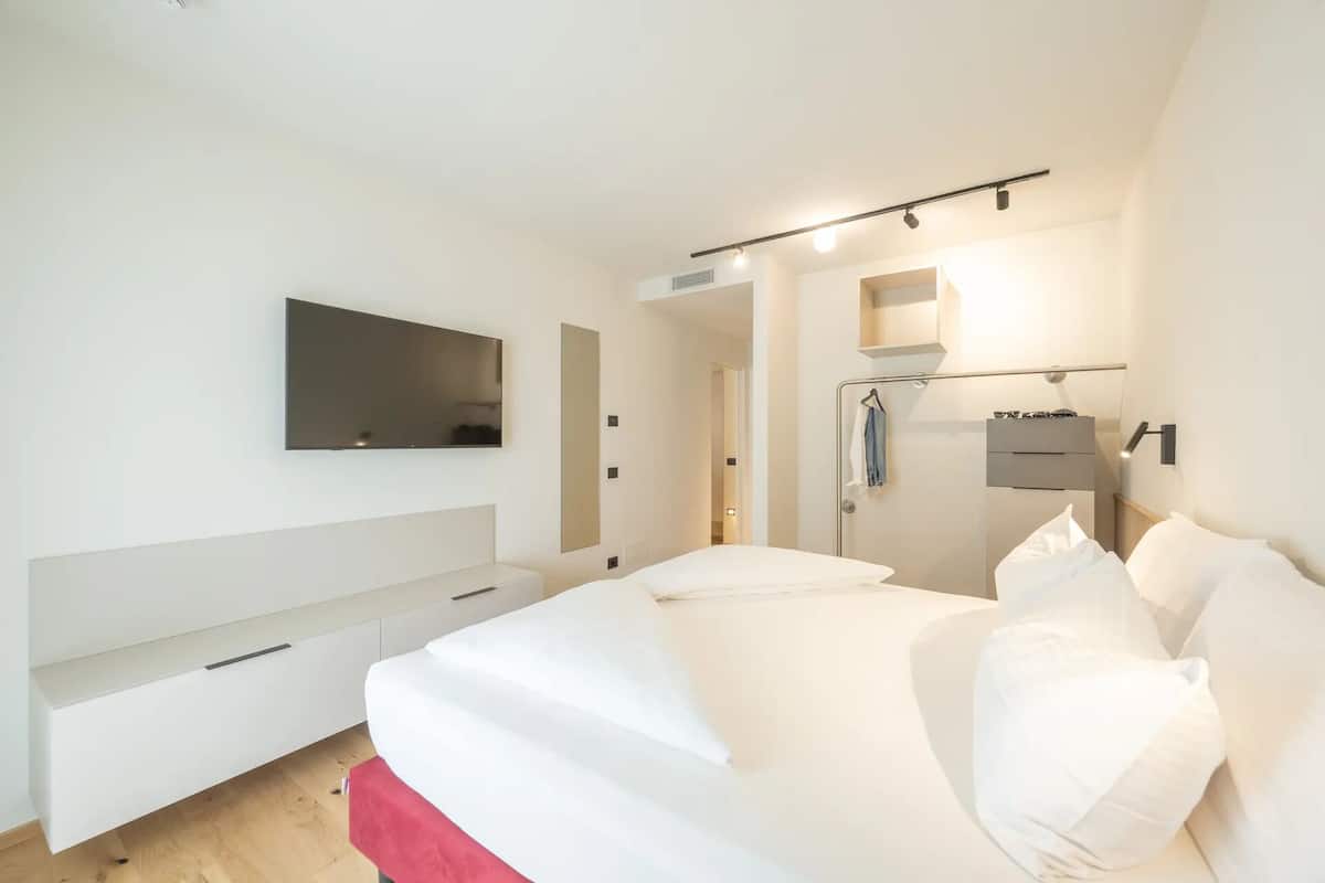 Une chambre à coucher avec un lit, un téléviseur fixé au mur, une armoire et un miroir.