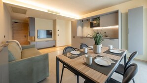 Un comedor moderno con una mesa de madera dispuesta para cuatro personas, un sofá y un televisor montado en la pared.