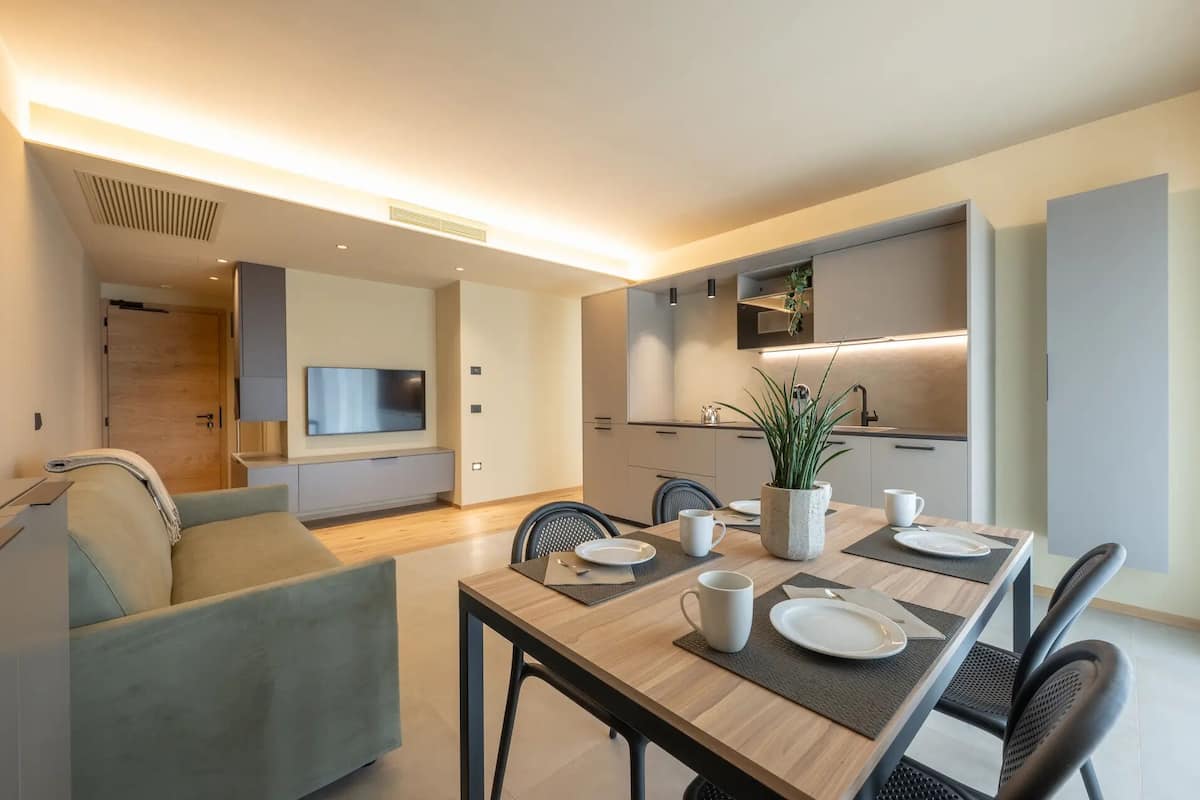 Un espace repas moderne avec une table en bois dressée pour quatre personnes, un canapé et un téléviseur fixé au mur.