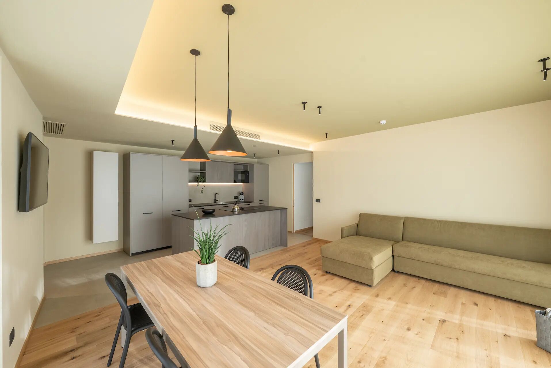 A modern kitchen with a dining area, a sofa, and a TV mounted on the wall.
