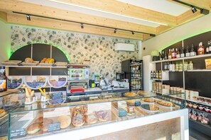 Eine Bäckertheke mit verschiedenen Backwaren, ein Selbstbedienungsbereich für Wein und eine Steinwand mit floralem Muster.