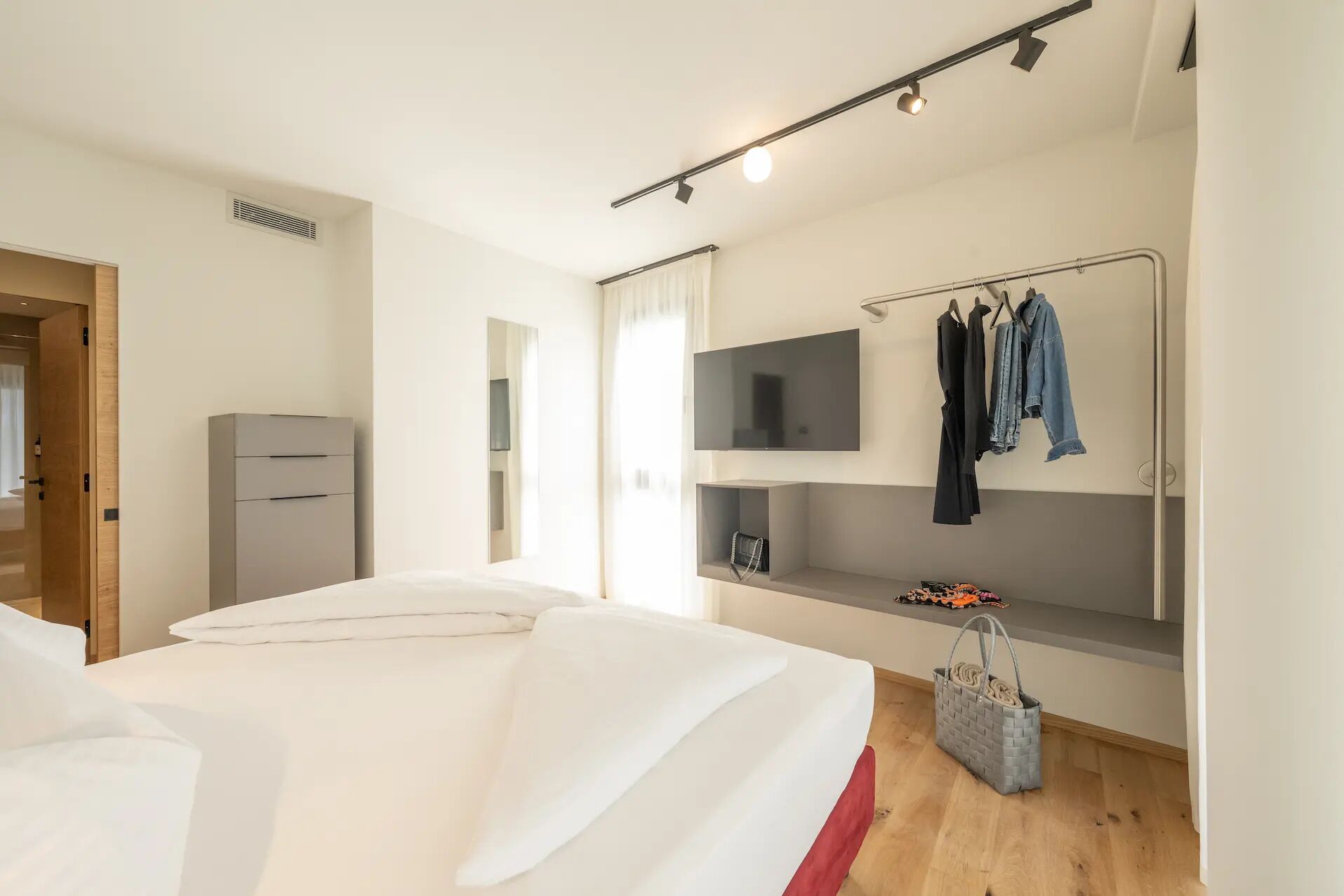 A modern bedroom with a bed, a TV, a wardrobe, and a clothing rack.