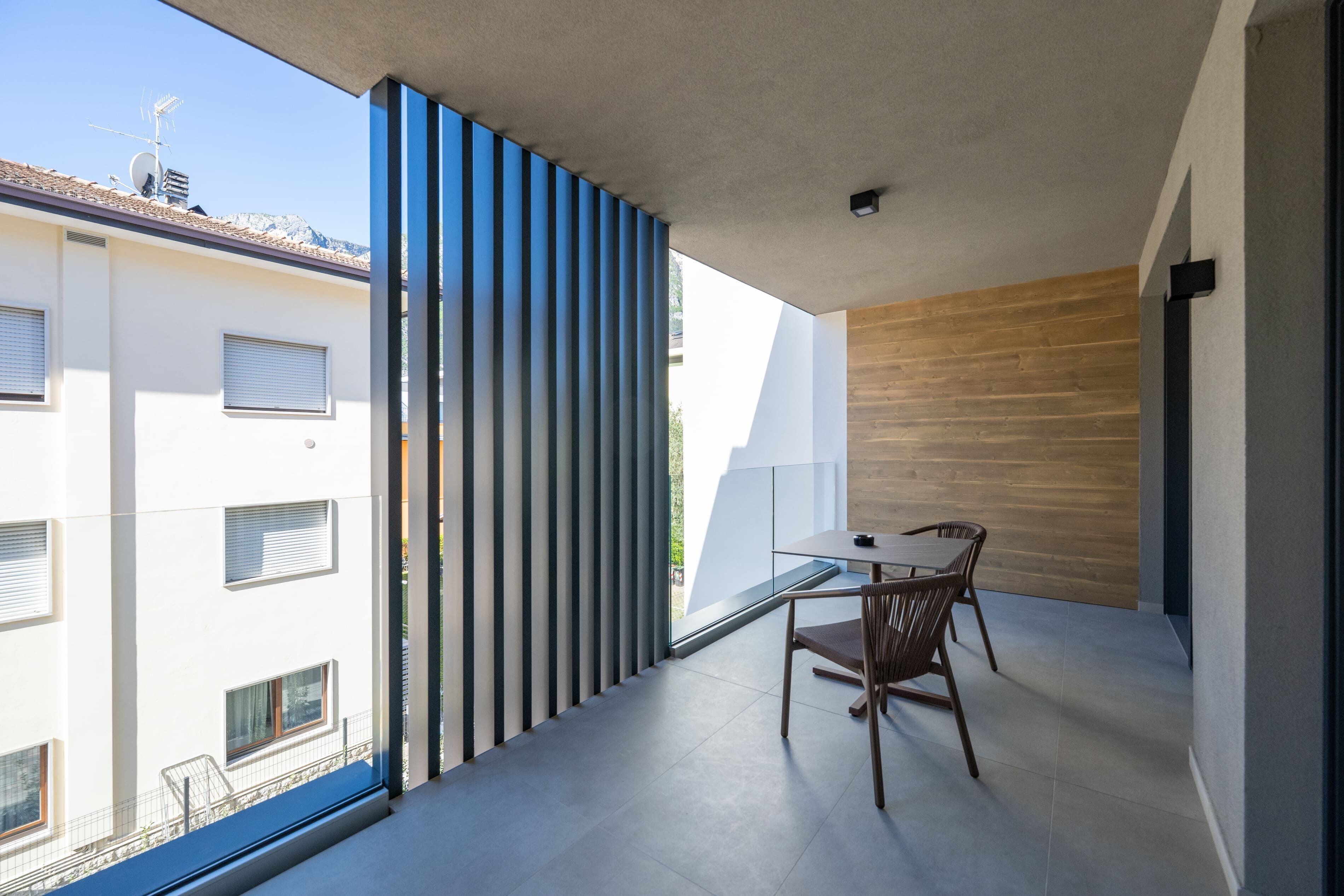 Un balcone con tavolo e sedie, vista sui palazzi circostanti e un muro in legno.