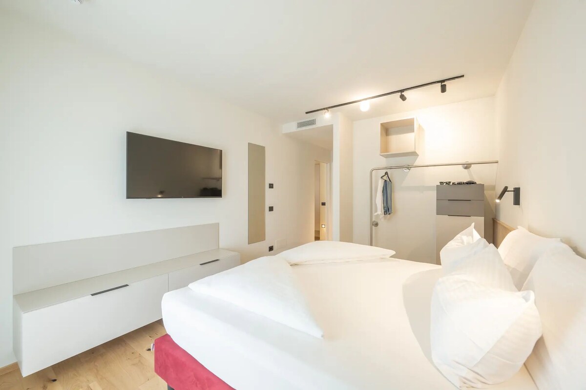 Une chambre à coucher avec un lit, un téléviseur fixé au mur, une armoire et un miroir.