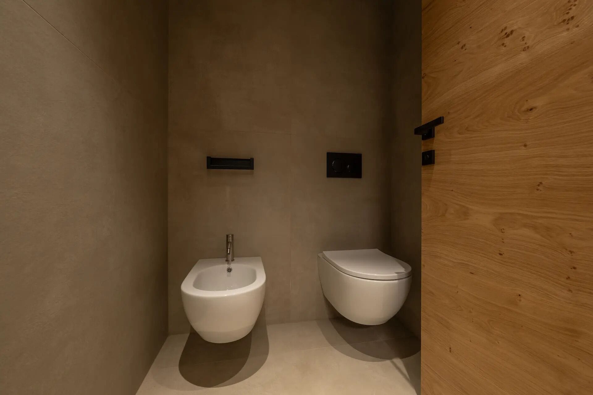 Een moderne badkamer met een bidet, toilet en houten lambrisering.