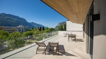 A balcony with a table and chairs, a glass railing, and a view of mountains.