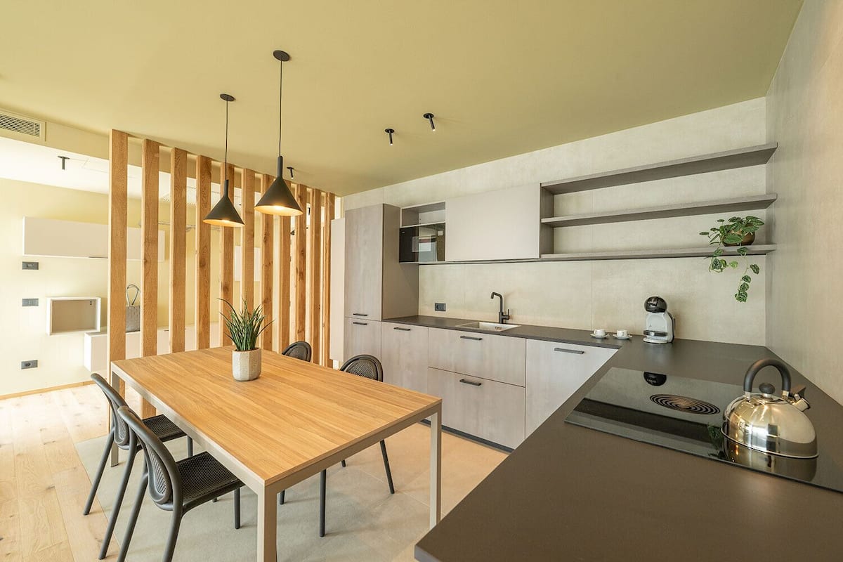 Une cuisine moderne avec une table à manger en bois, des luminaires suspendus et une bouilloire.