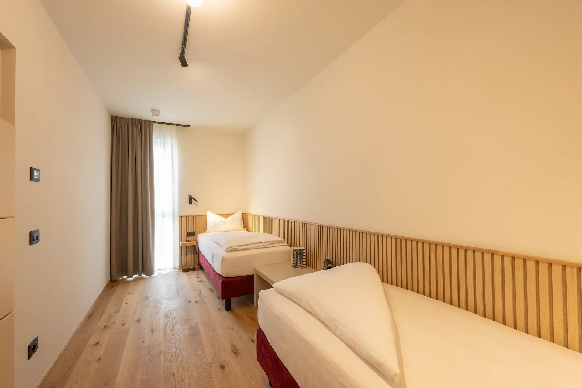 Une chambre d’hôtel avec un plancher en bois, un lit avec une literie blanche, une table de chevet et une fenêtre avec des rideaux.