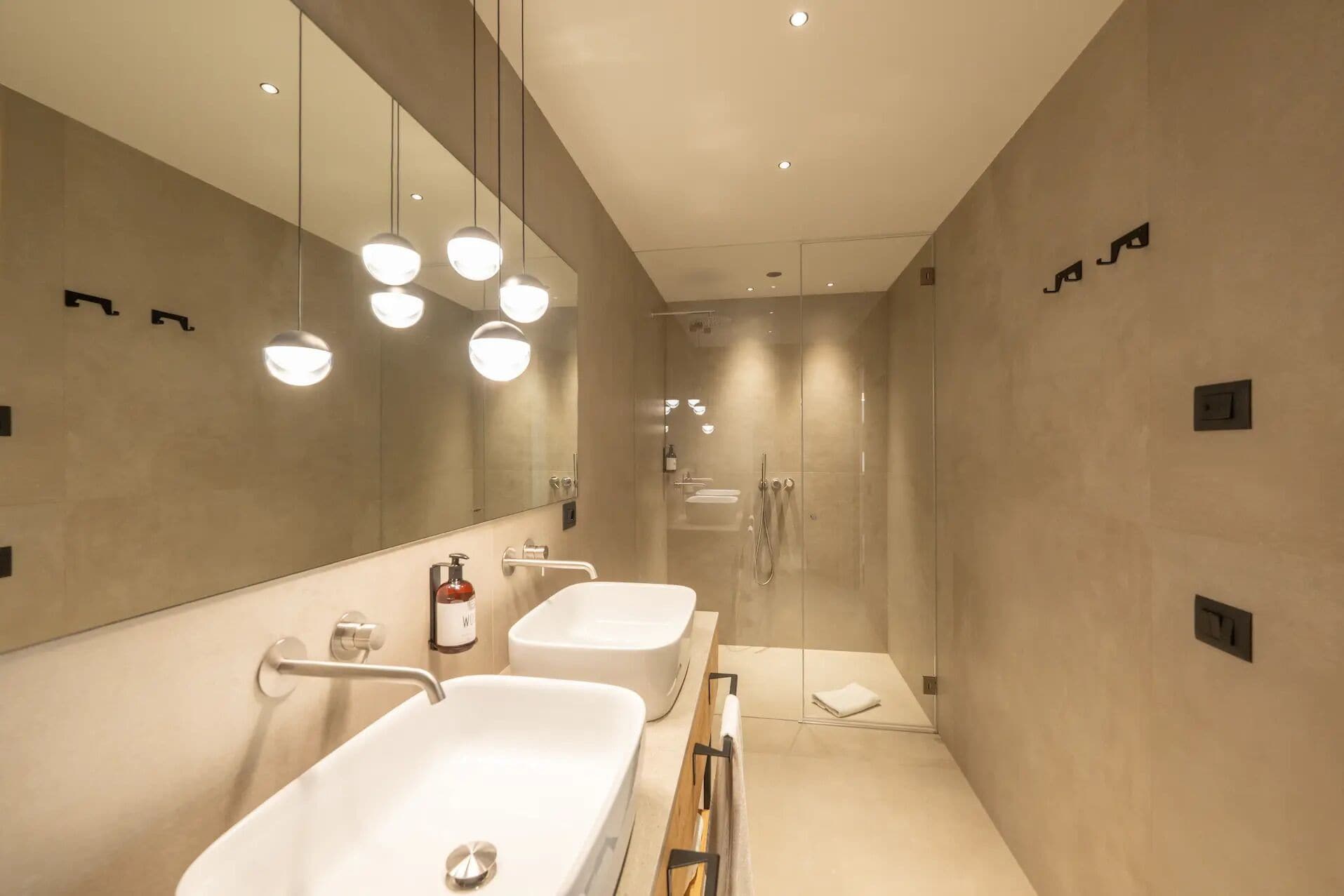 A modern bathroom with two sinks, a large mirror, and a glass-enclosed shower.