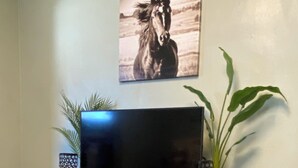 En platt-TV står på ett vitt träbord, och bredvid den finns två dekorativa vaser, en målning av en häst och en stor grön växt.