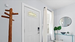 A hallway with a white door, a wooden coat rack, a glass console table with a plant, and a round mirror. - The Sheridan Family Compound 4BR + 2.5BA (Detroit)