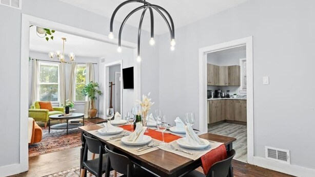 A dining area with a wooden table set for four, a modern chandelier, and a view into the adjacent living room and kitchen. - The Sheridan Family Compound 4BR + 2.5BA (Detroit)