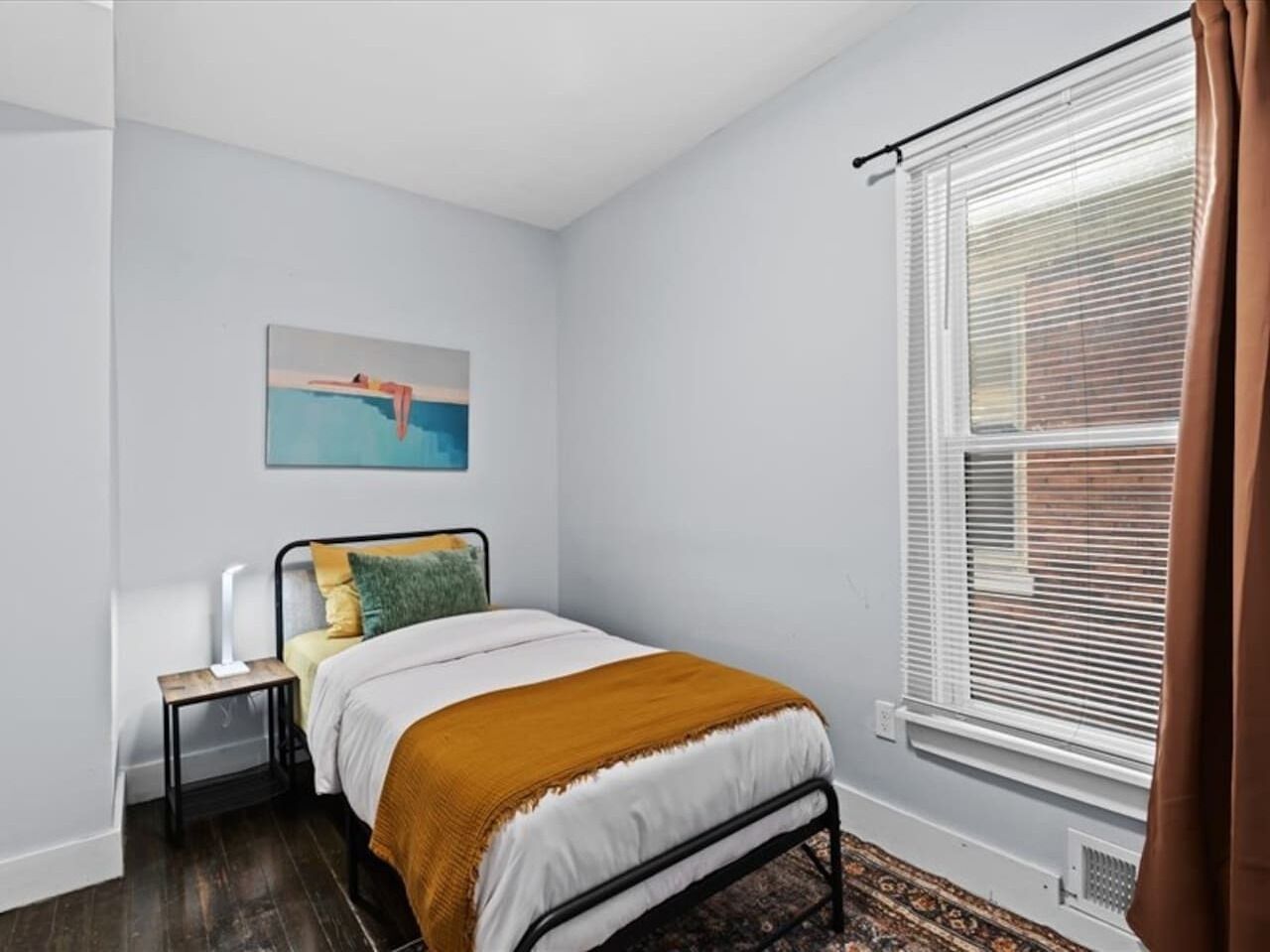 A bedroom with a bed, bedside table, lamp, and a painting on the wall.