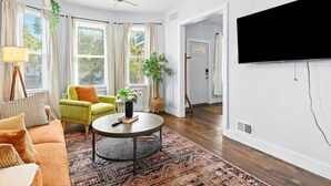 A living room with a sofa, armchair, round coffee table, and a television mounted on the wall. - The Sheridan Family Compound 4BR + 2.5BA (Detroit)