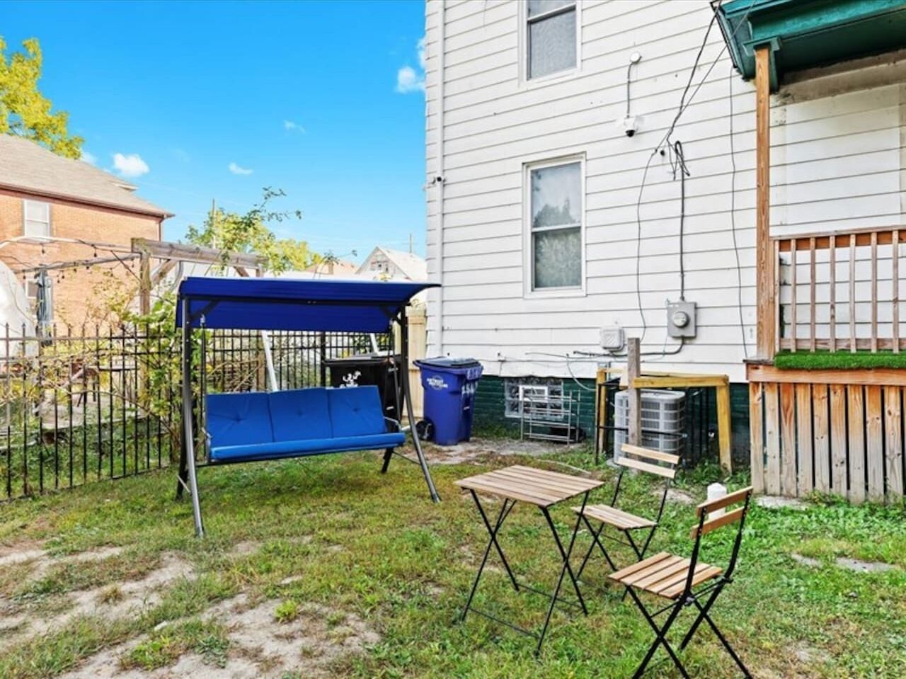 A backyard with a blue swing set, a wooden table, and two chairs.