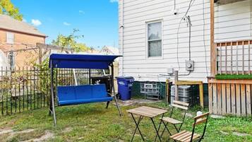 A backyard with a blue swing set, a wooden table, and two chairs.