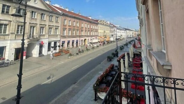 A street view with buildings, a clear sky, and a balcony with red chairs. - Fantastic Inn Warsaw - NS38 (Warsaw)