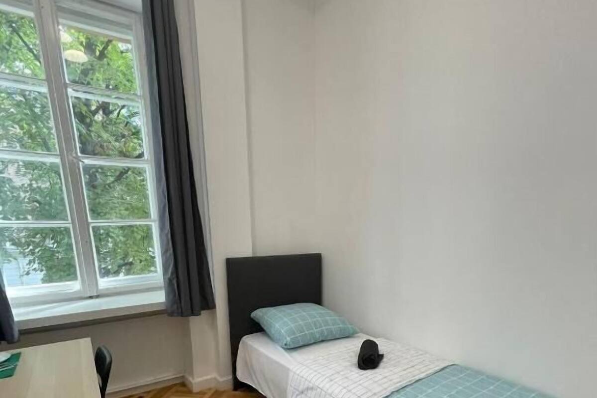 Egy hálószoba, amelyben van egy ágy, egy íróasztal és egy ablak, amelyen függöny van.