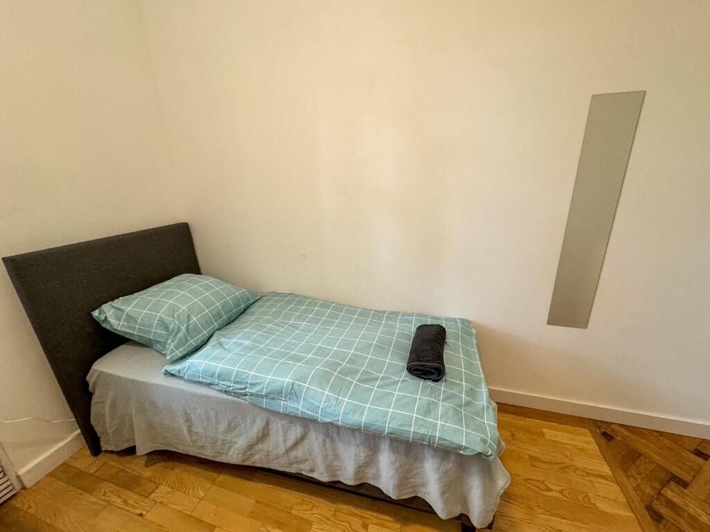 A small, single-bed room with a dark headboard, a light-colored mattress, and a teal checkered bedspread.