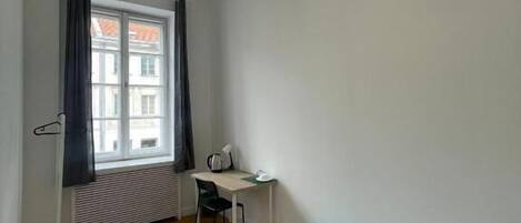 Ein kleiner, schlicht eingerichteter Raum mit einem Bett, einem Schreibtisch und einem Heizkörper.