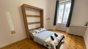 A bedroom with a wooden bed frame, a floral bedspread, and a window with curtains. - Fantastic Inn Warsaw - NS38 (Warsaw)