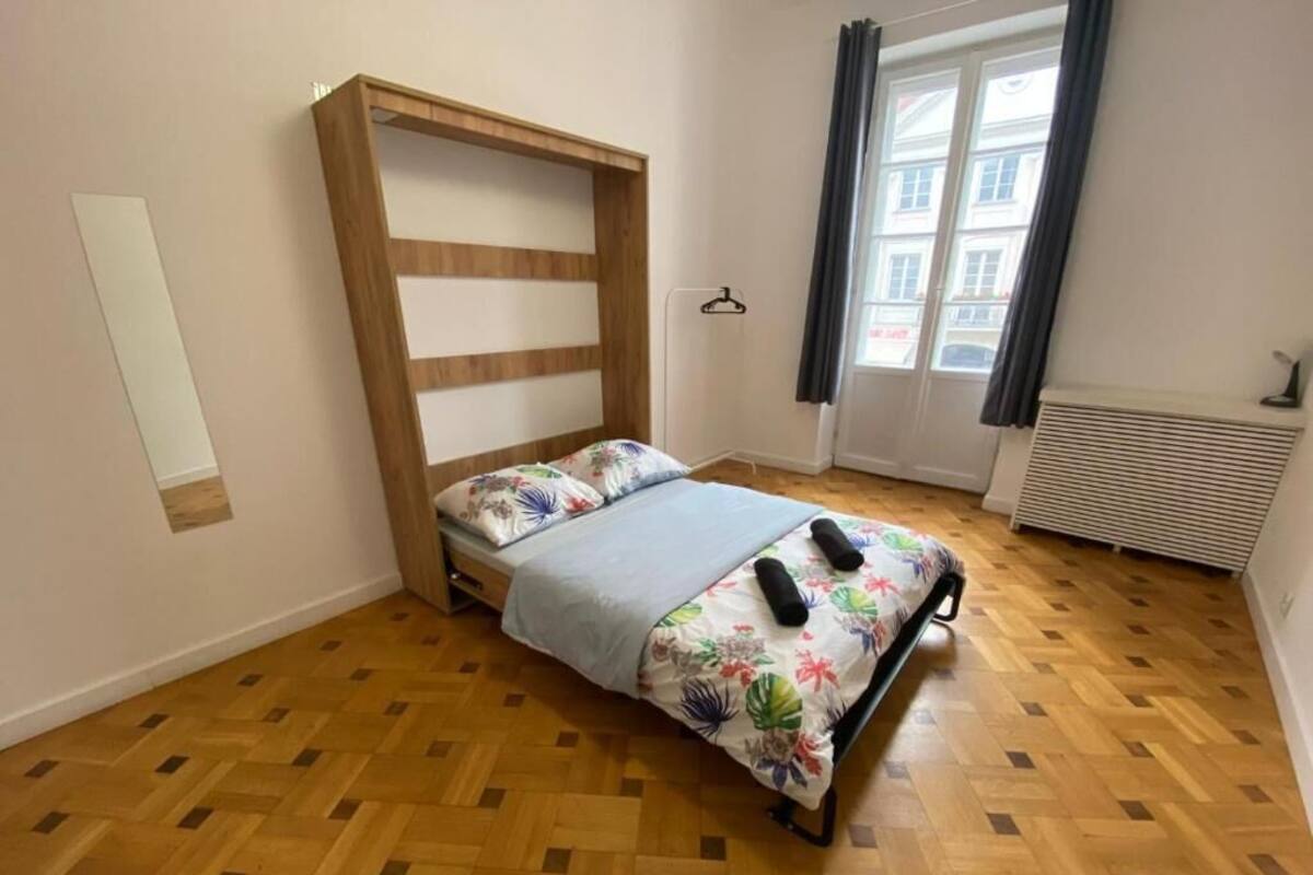 Egy hálószoba, amelyben egy fa ágykeret, virágmintás ágytakaró és függönnyel ellátott ablak található.
