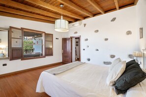 Ein Schlafzimmer mit Holzboden, einem Bett mit weißer Bettwäsche, einem Spiegel und einer Steinwand.