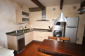 A compact kitchen with a dishwasher, oven, microwave, and a wooden dining table.