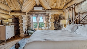 A log cabin bedroom with a large bed, a dresser, a chair, and a small table. - Spruce Moose Lodge, Custom Log Cabin with Hot Tub (Hartland)